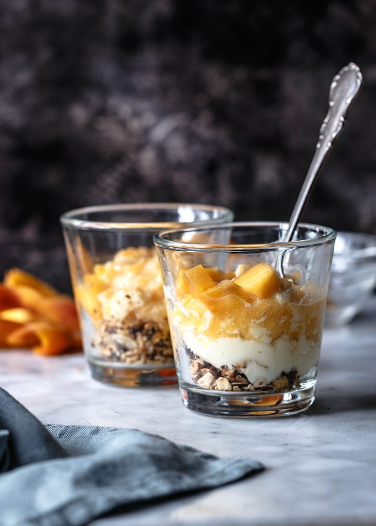 Melocotón cheesecake en vaso con crema de queso y base de granola de chocolate.